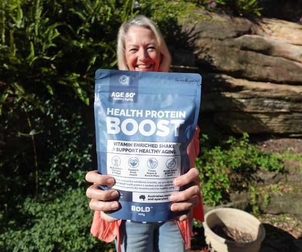 Smiling woman holding a pouch of BOLD Health Protein Boost outdoors