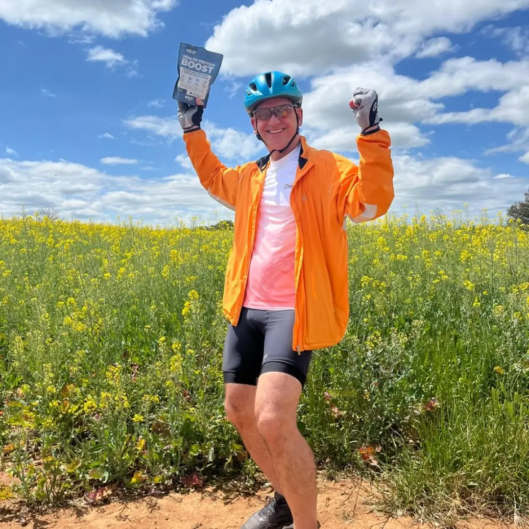 Cyclist celebrating in canola field with Health Protein Boost