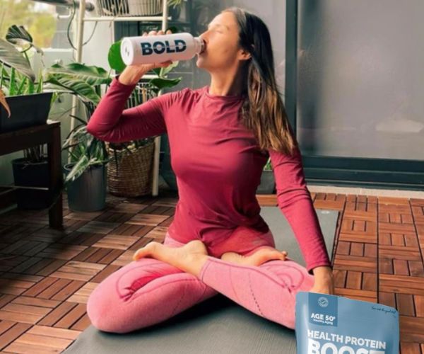 Woman seated on a yoga mat drinking from a BOLD shaker